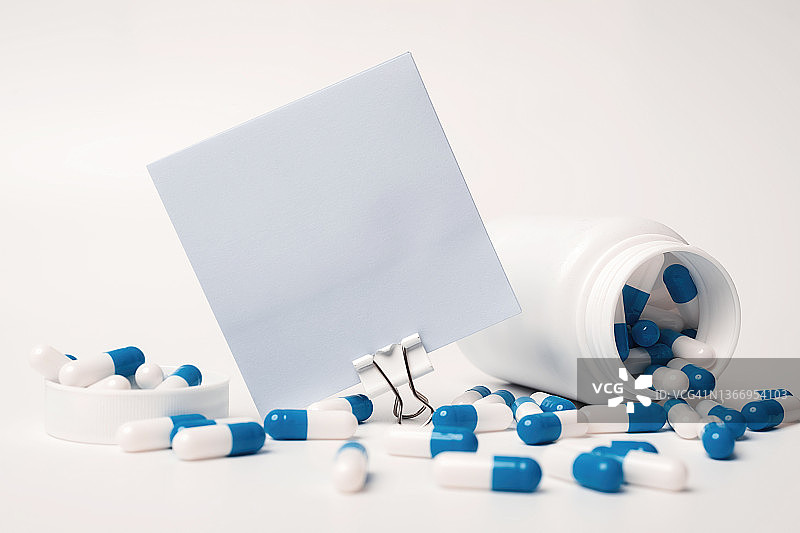 一张空白的蓝色方块便签和蓝白色药丸从药瓶中溢出的特写。医学概念。为未来重要事件公告留出空白图片素材