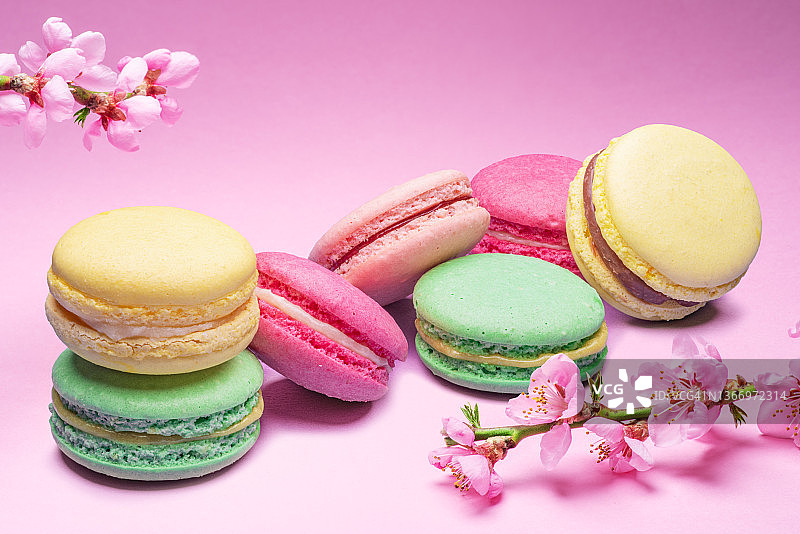 五颜六色的甜马卡龙或马卡龙，粉红色背景的风味饼干，旁边是盛开的樱桃枝。图片素材