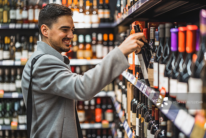 在超市里，一个微笑的帅哥手里拿着一瓶酒图片素材