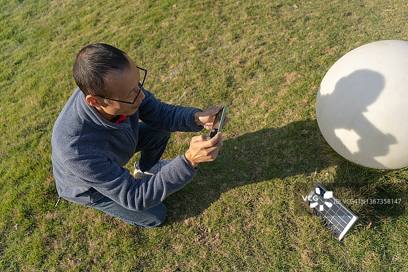 男子用手机拍摄草坪上路灯的太阳能电池板图片素材
