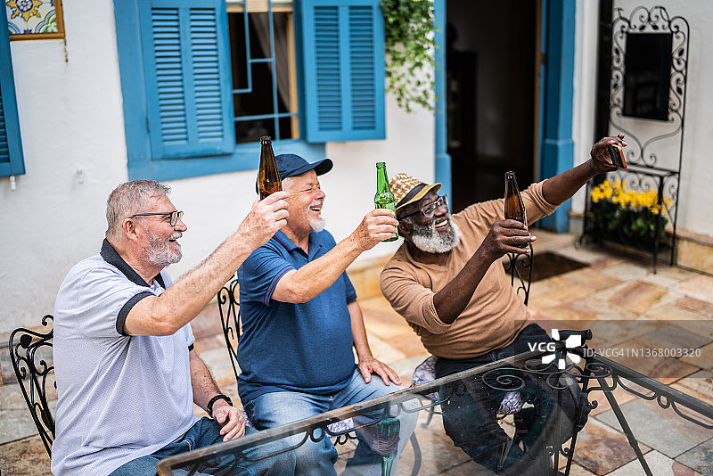 老年男性一边喝啤酒一边用手机拍摄或视频通话图片素材