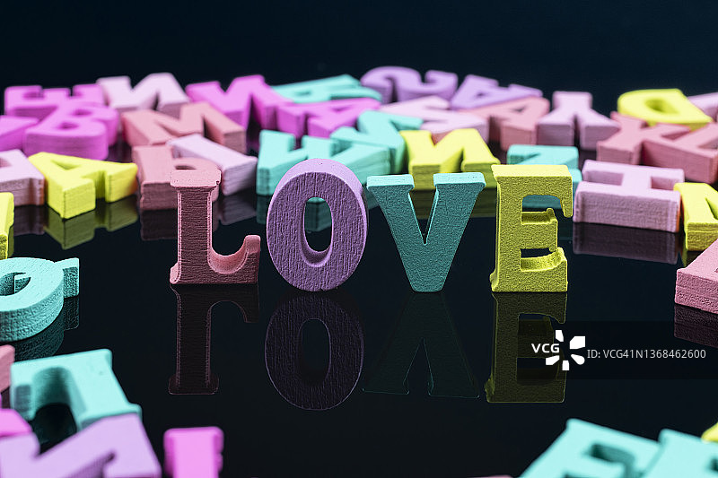单词-爱-拼写与彩色木制字母在黑色背景图片素材