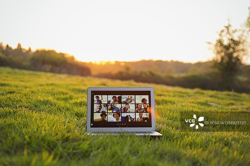 朋友们在阳光明媚的草地上用笔记本电脑屏幕视频聊天图片素材