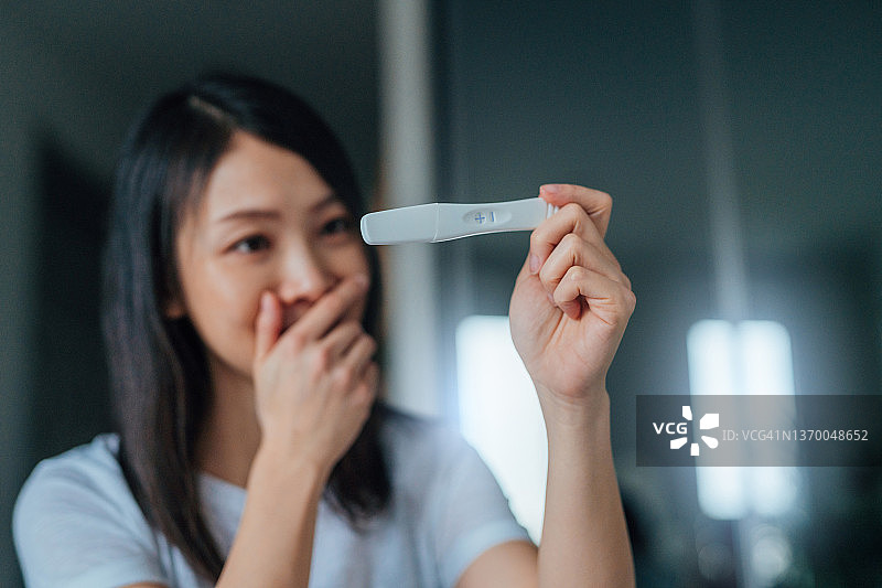快乐的年轻亚洲妇女拿着家里的怀孕测试试剂盒图片素材