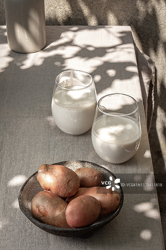 土豆奶替代非乳制品健康素食饮料在花园里的桌子上与树影。阳光图片素材