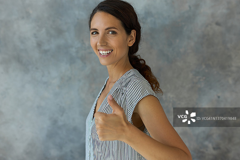 室内肖像微笑积极的女性与波波浪的头发摆姿势与拇指半转向相机对工作室墙壁与你的广告内容复制空间。肢体语言图片素材