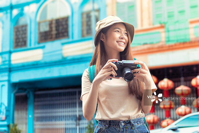 年轻的女游客用老式相机在城市里开心地微笑着。快乐的年轻女人，带着城市地图，背着背包旅行图片素材