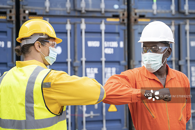 疫情期间，两名戴口罩的工程师在一个大型贸易港口用肘部相互问候。图片素材