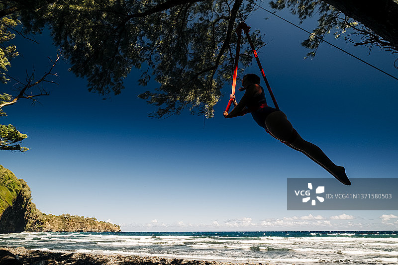 一名女子在夏威夷热带海滩上的空中丝绸吊床上表演图片素材
