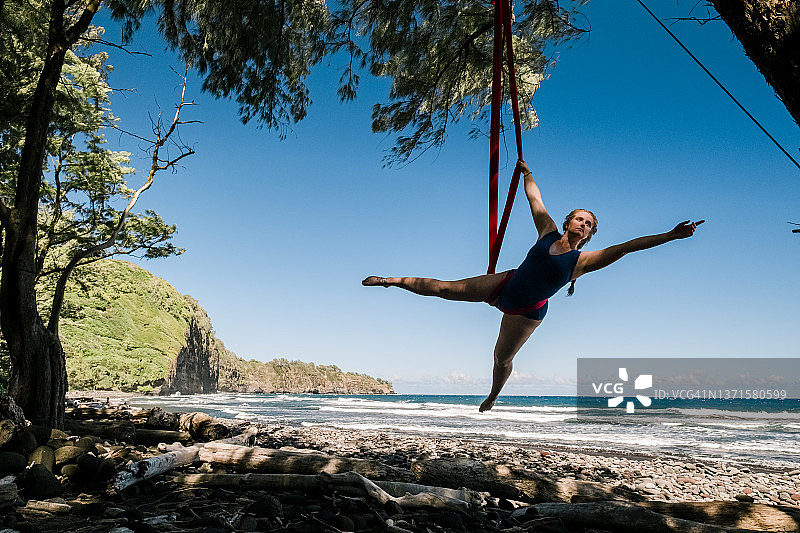 一名女子在夏威夷热带海滩上的空中丝绸吊床上表演，她在空中飞行图片素材