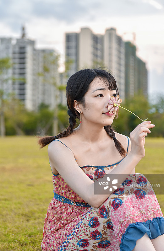 一位优雅的亚洲女孩(25 ~ 29岁)在中国广东江门的公园里闻着鲜花。图片素材