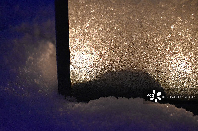 雪花和一盏点亮的灯笼的一部分，窗户上覆盖着冰晶。图片素材