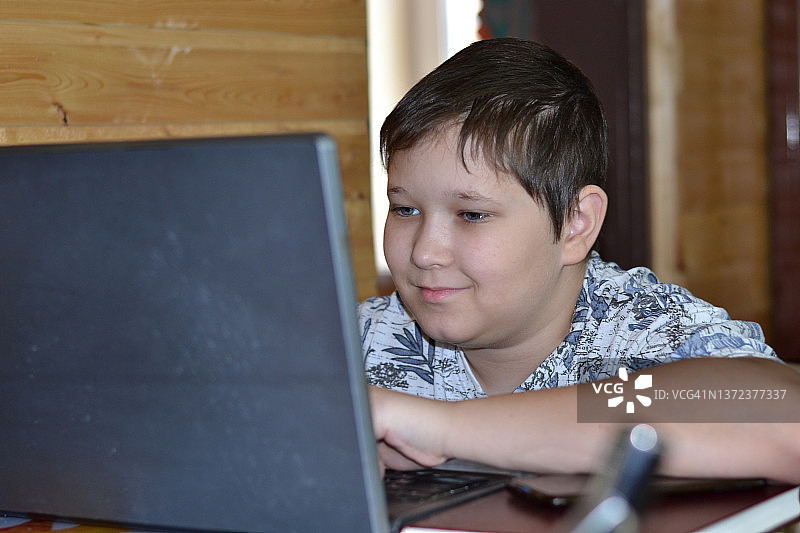 一个十几岁的男孩在用笔记本电脑。图片素材