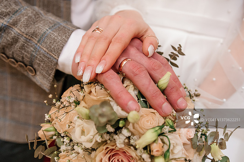 新婚夫妇的手，戴着金戒指和一束鲜花。新郎新娘的手放在一束漂亮的花束上图片素材