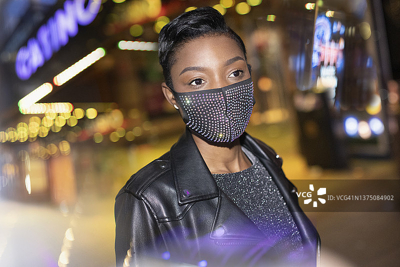 戴着闪亮面具的年轻女子在夜晚灯火通明的城市里图片素材