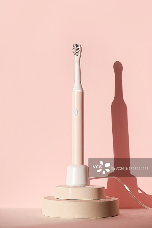 新型现代超声波牙刷。在粉红色粉彩背景的圆柱平台上的牙科护理用品。口腔卫生，牙齿和牙龈健康，牙齿健康。牙科产品图片素材