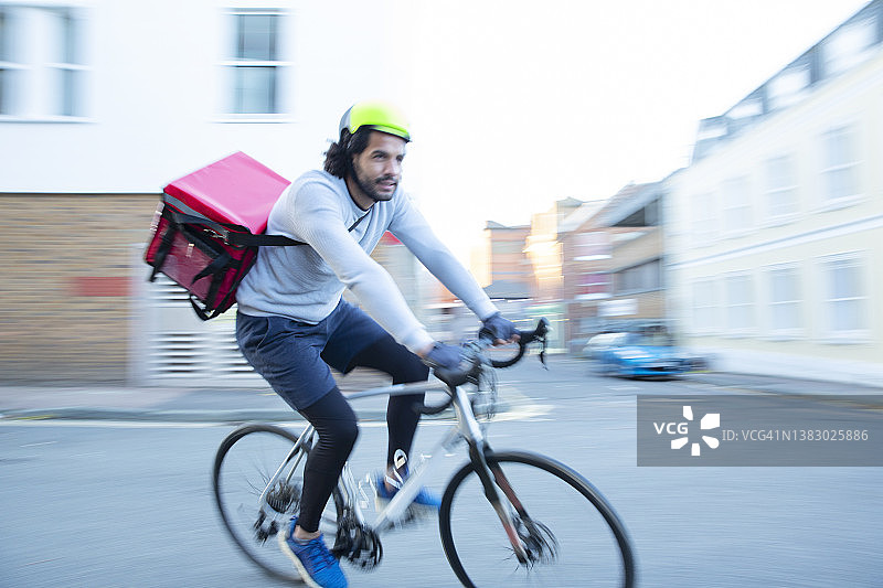在城市附近骑自行车送食物的男性邮递员图片素材