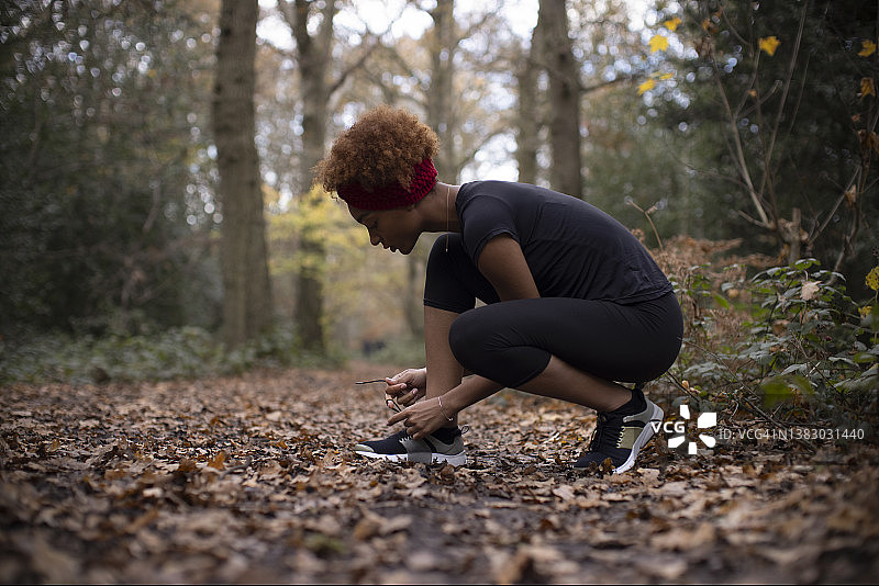 年轻的女跑步者在秋天的树林里系鞋带图片素材