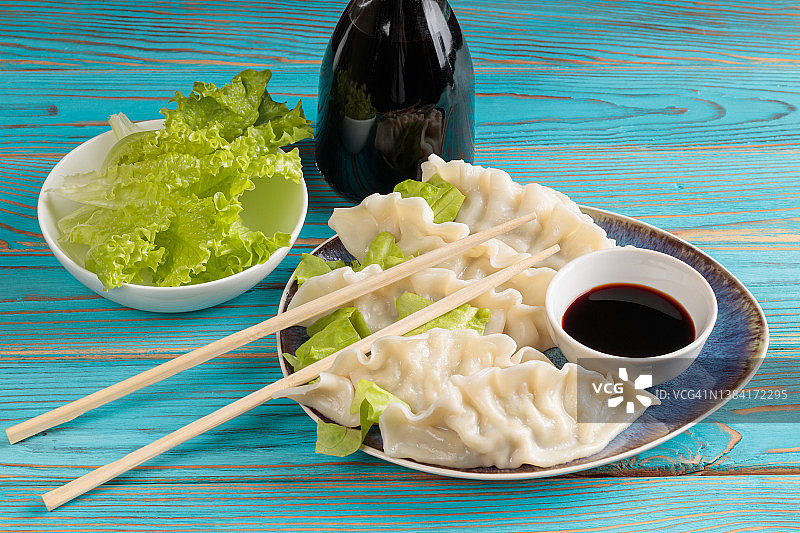 新鲜煮熟的中国饺子与酱油和绿色沙拉在蓝色木制背景。图片素材