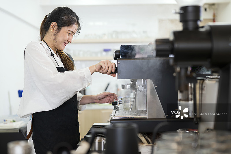 煮咖啡的感觉太棒了。侧视图的一个亚洲女性咖啡师工作在咖啡馆和准备咖啡从咖啡机为顾客服务。图片素材