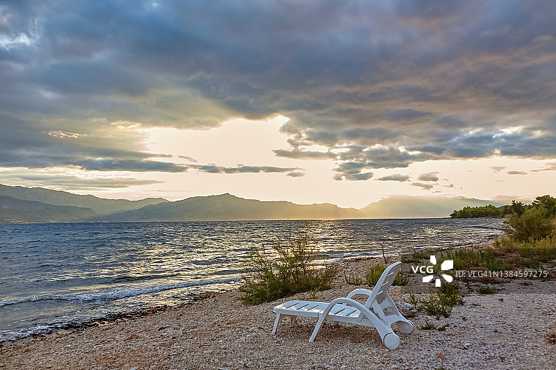 旅游度假区沙滩上草伞下的折叠式躺椅。图片素材