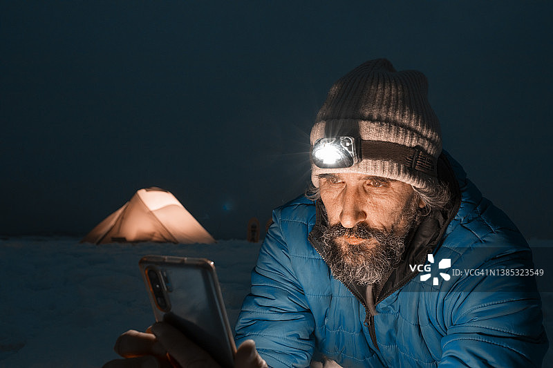 成熟的游客在冬山露营时使用手机，独自在大自然中。图片素材