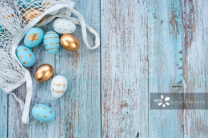 金色，黑色，白色，蓝色的鸡蛋在一个蓝色的木制背景的绳袋。几何学。最小的概念。前视图。复活节卡片，上面有文字的地方。图片素材
