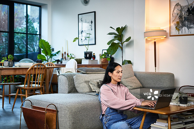 成熟的中国女人坐在客厅地板上使用笔记本电脑，在家工作图片素材