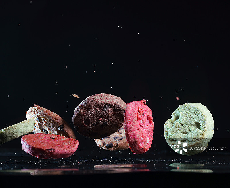 彩色的巧克力饼干在黑色背景的半空中飞行图片素材