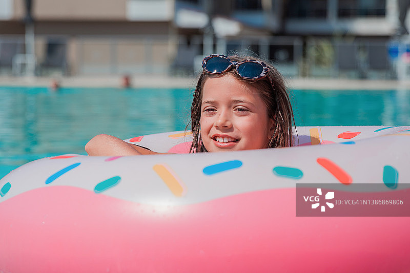 快乐的女孩从一个充气甜甜圈形状的环在游泳池里偷看图片素材