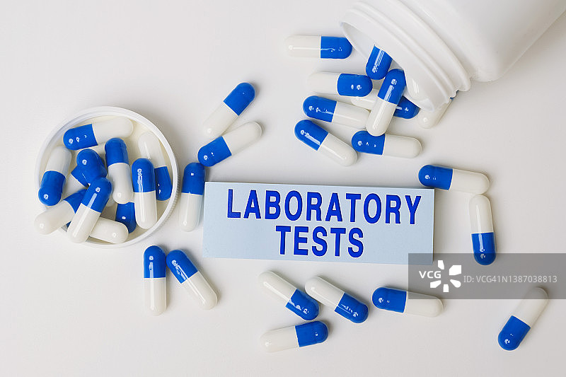 实验室测试——从药瓶中溢出的蓝白色药丸旁边的纸上有铭文。医学的概念图片素材