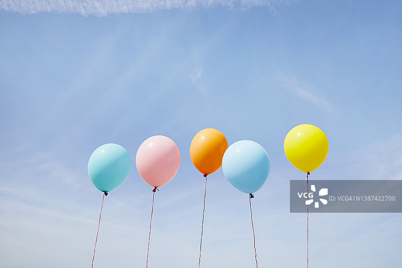 在蓝天的衬托下，五个彩色气球排成一排图片素材