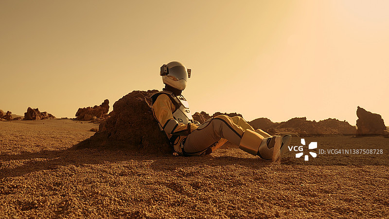 在火星上的孤独。女宇航员探索铁锈色的洞穴和岩石。坐在岩石上图片素材