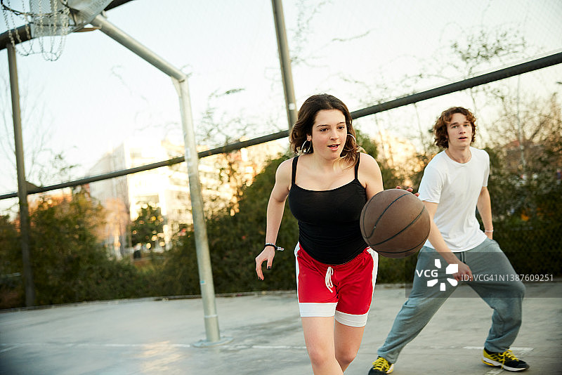 一个年轻女子把球运向篮球框。图片素材