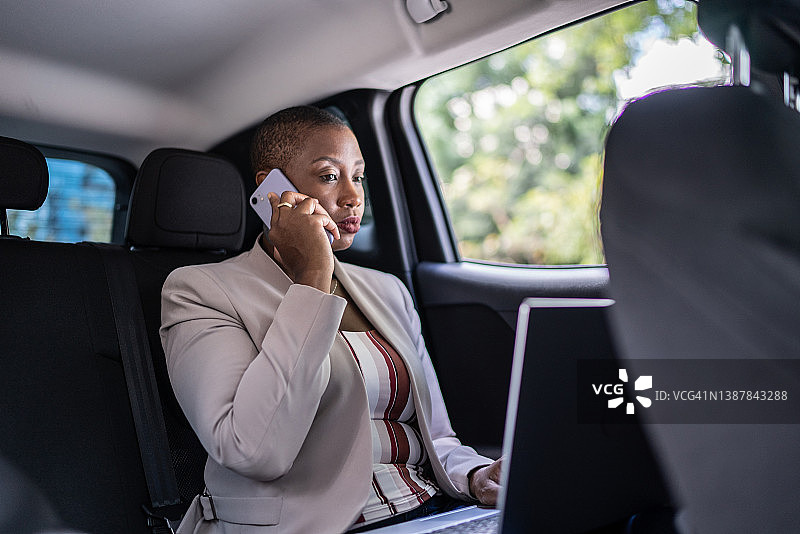 女商人在车里一边讲手机，一边用笔记本电脑图片素材