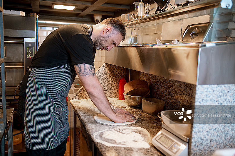 在餐厅厨房的柜台上，一名男子正在揉披萨面团图片素材