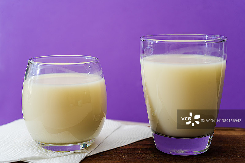 两杯不同形状和体积的牛奶放在桌子上的木板上。健康的饮料。高观点图片素材