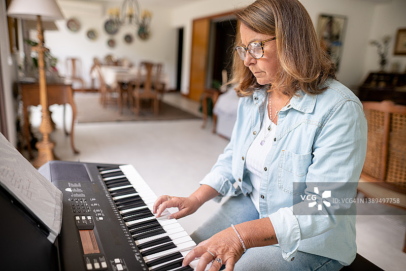 一个成熟的女人在她的客厅里玩电子键盘图片素材