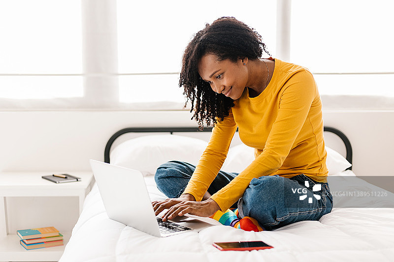 年轻的非洲裔美国妇女坐在家里的床上使用笔记本电脑。图片素材