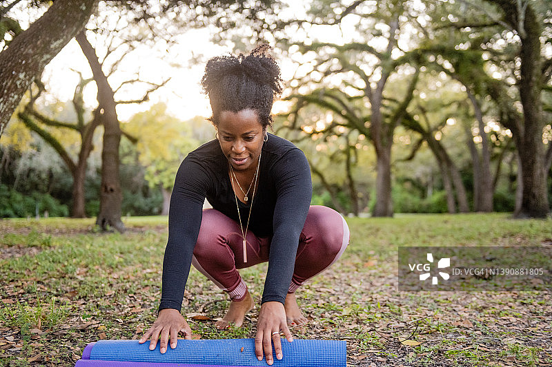 一个有着自然黑发的女人在公园里卷起她的瑜伽垫图片素材