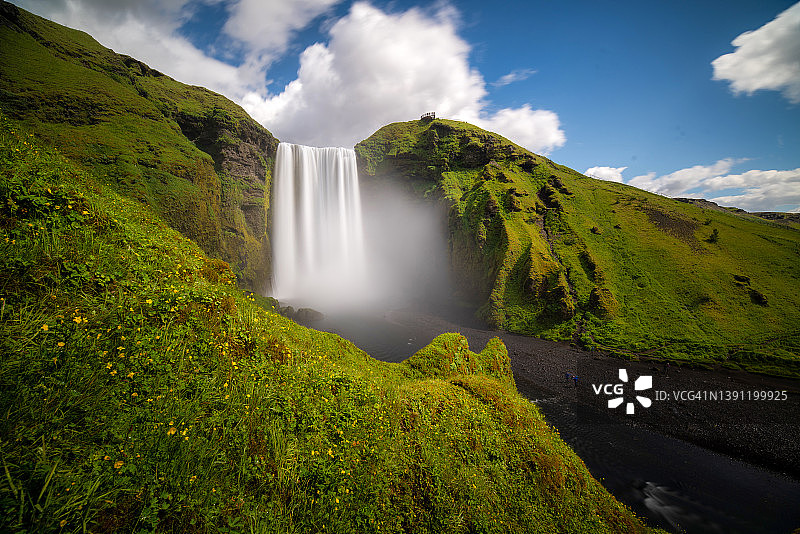 夏日里，天空湛蓝的冰岛斯科加佛斯瀑布。Skógafoss瀑布是冰岛的热门景点之一，深受冰岛中南部游客的喜爱。图片素材