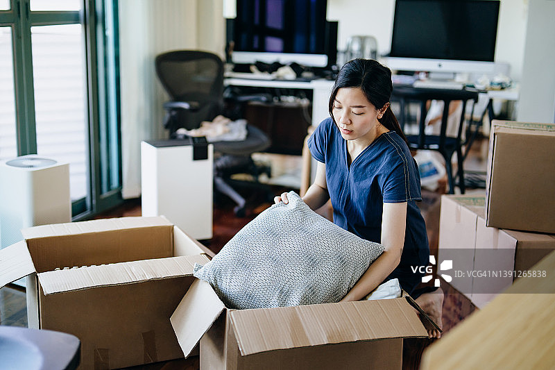 年轻的亚洲女性搬进新公寓。在客厅将物品装箱或拆箱。搬家、迁移、搬迁的概念图片素材
