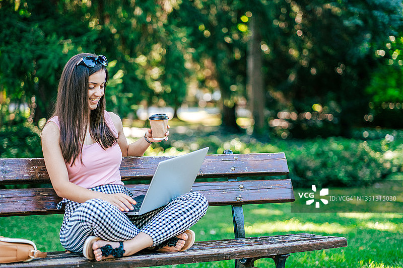 一个年轻漂亮的女人坐在公园里用笔记本电脑学习图片素材