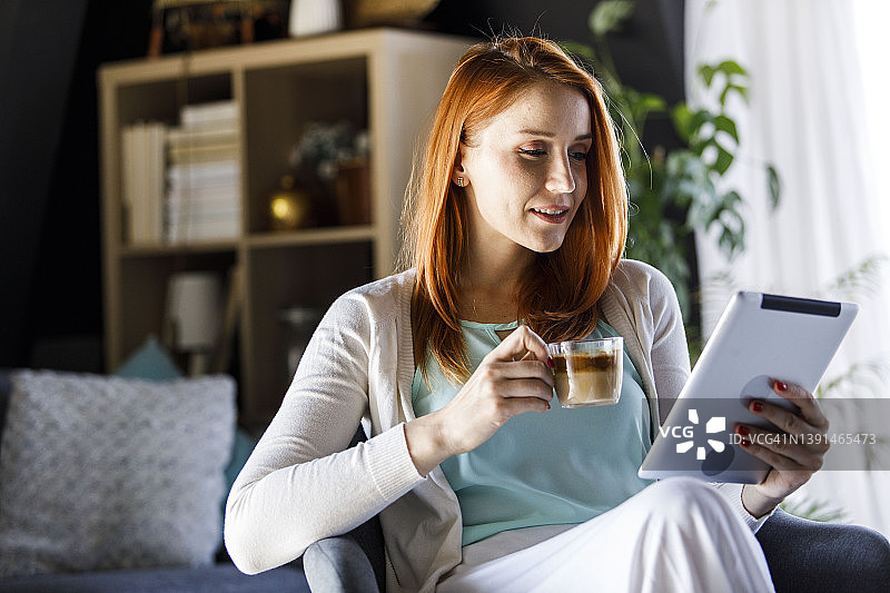 复制一个年轻的红发女孩早上喝咖啡用数码平板电脑的照片图片素材