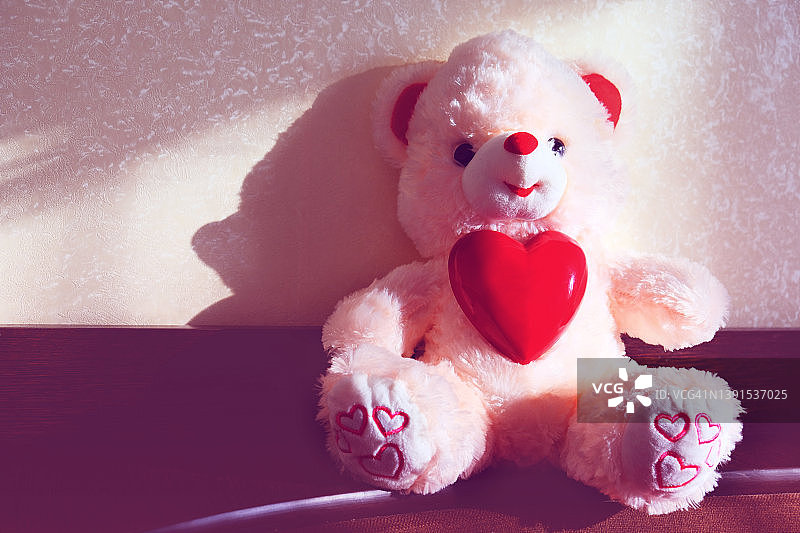 有一颗心的玩具熊。准备一个浪漫的假期在家，柔和的晨光。情人节，生日和爱的概念图片素材