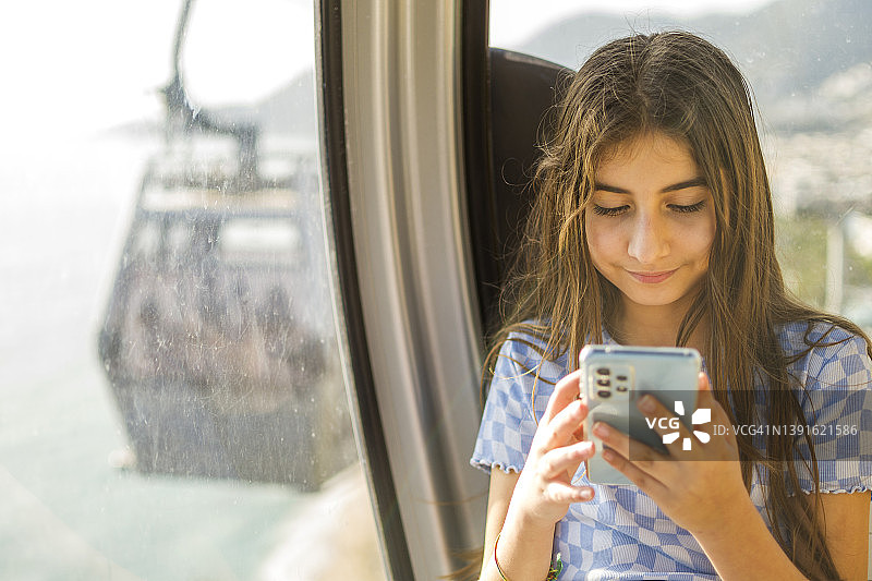 漂亮的小女孩在缆车上用手机图片素材