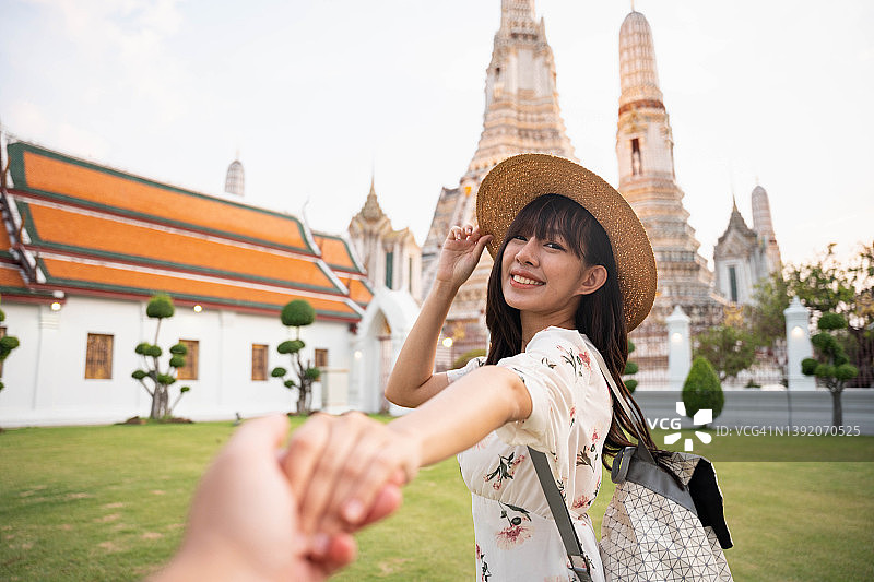 年轻美丽的女人在曼谷寺庙旅行期间握着男朋友的手的后视图。图片素材
