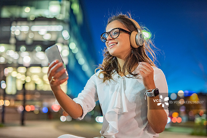 在城市里，女人晚上戴着耳机听音乐图片素材