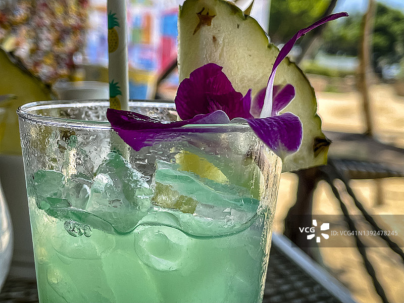 水绿色彩色异国情调的热带鸡尾酒在阳光海滩旅游胜地设置甲板椅子看海洋日落日出。旅游，旅游，健康和放松营销主题的概念片。图片素材