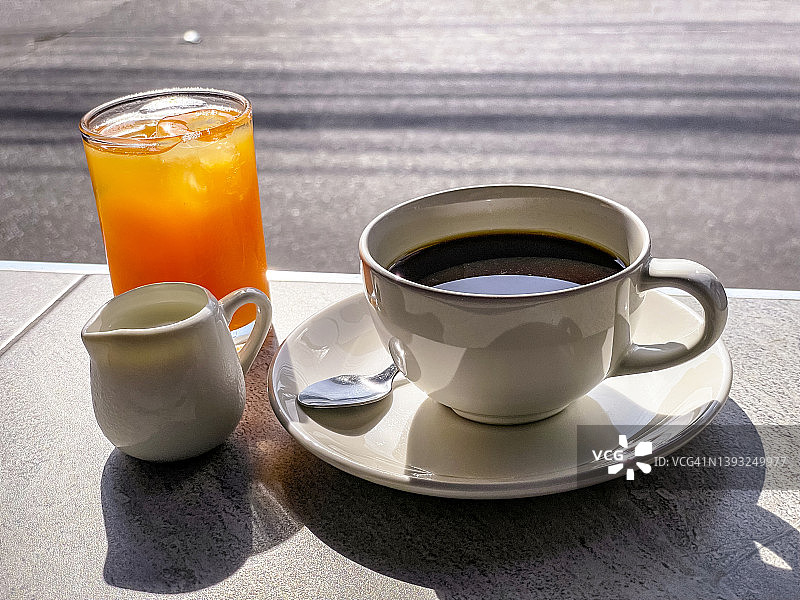 哀悼早餐例行的黑咖啡和橙汁在曼谷的城市街道在清晨高峰时间通勤交通。在享受一顿美味的早餐的同时，摩托车、汽车和嘟嘟车污染了交通。图片素材